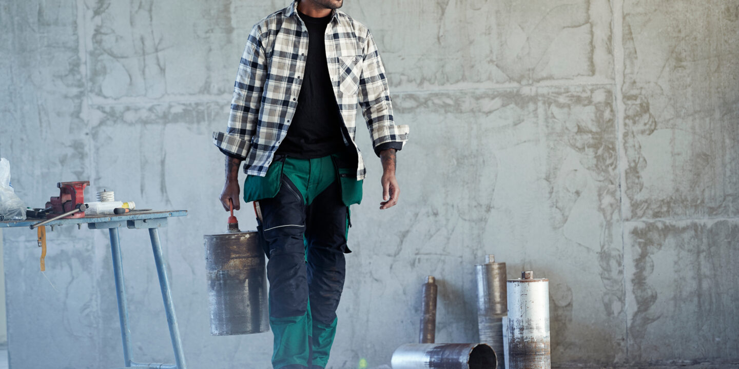 Image of a man wearing a checked shirt and workwear trousers in an industrial setting